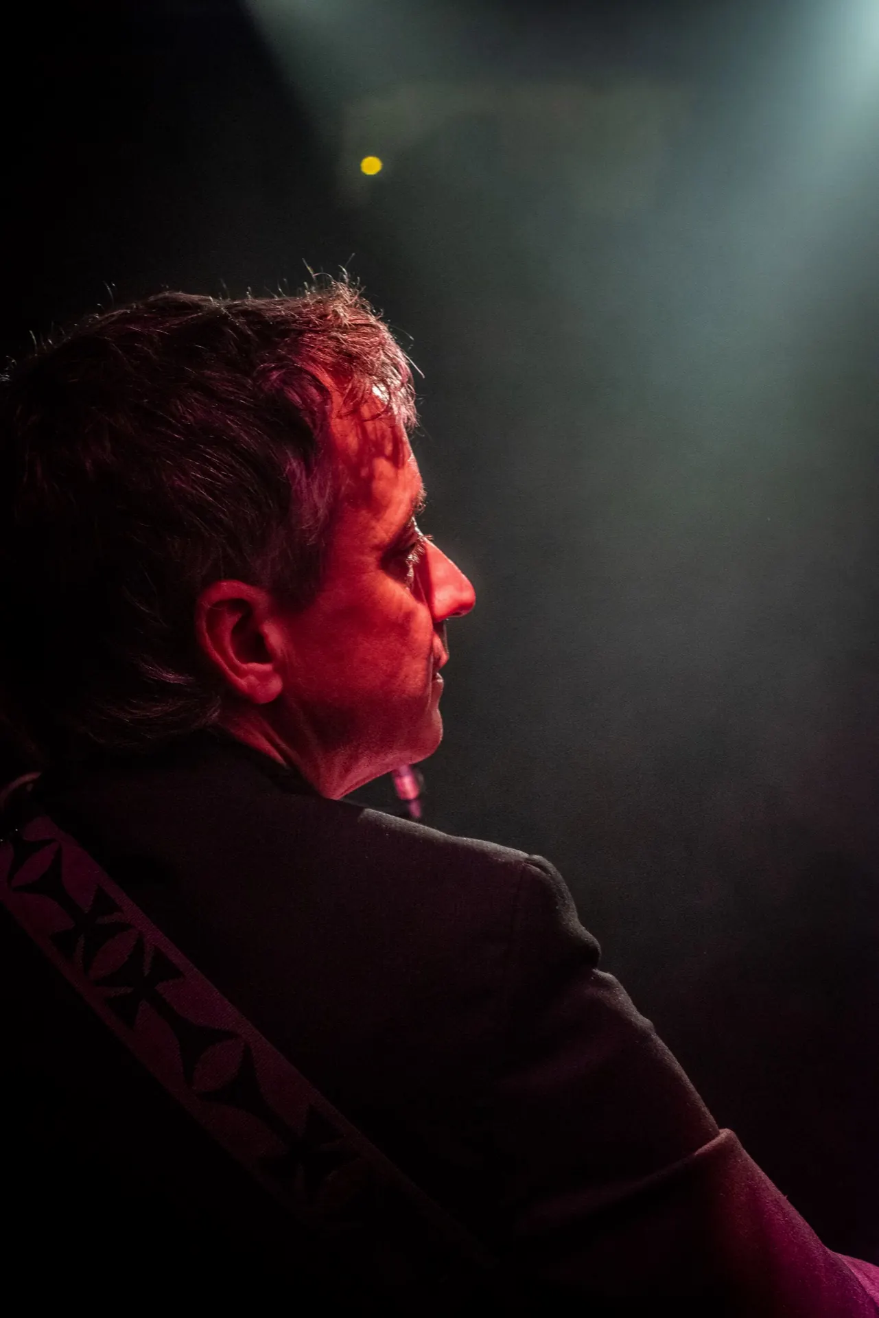 Profil de tête d'un musicien liseré de rouge, fond noir et fumée légère.