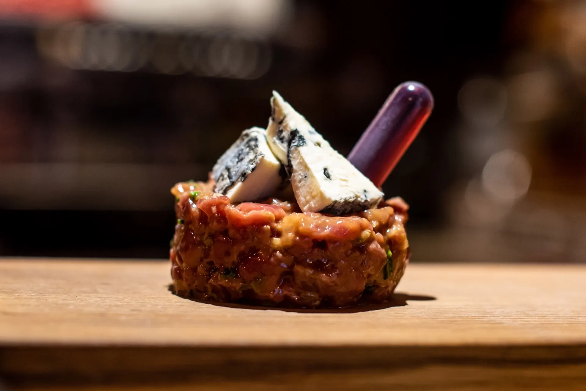 Tartare de bœuf coiffé de bleu, dressé dans la lumière chaude de la salle