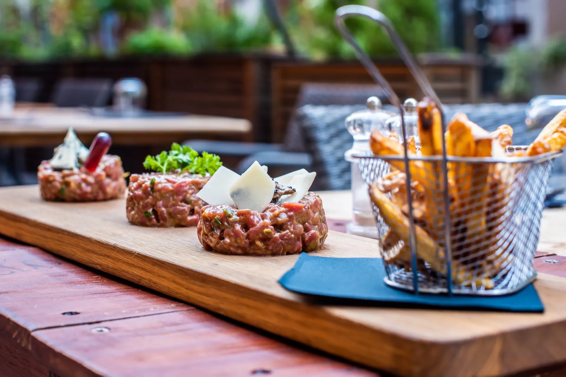 Trois tartares de bœuf sur planche avec panier de frites, servis en terrasse