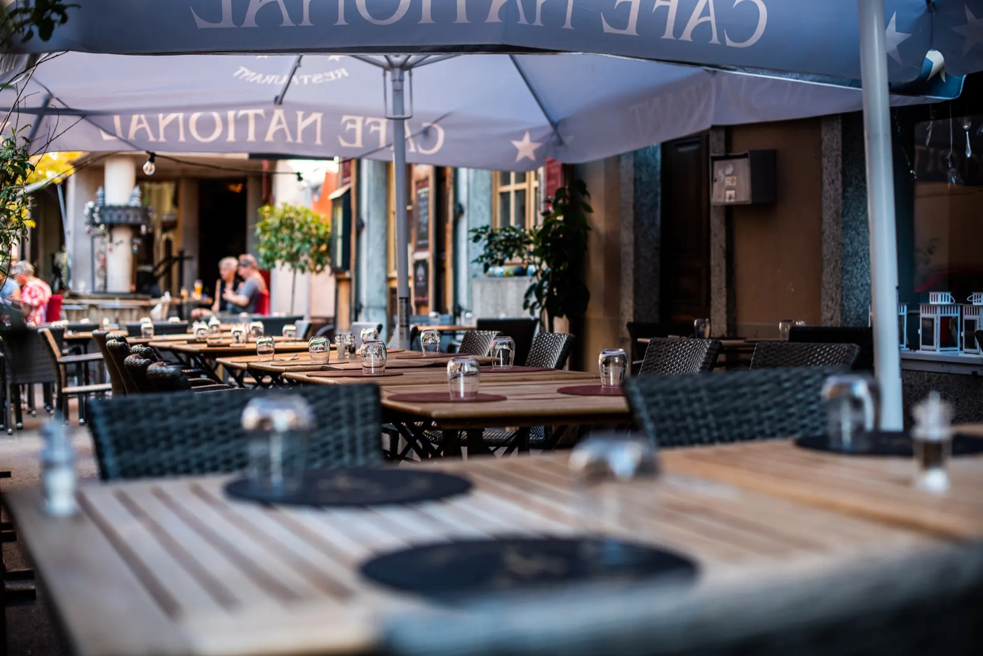 Tables dressées en terrasse du Café National sous les parasols, en début de soirée