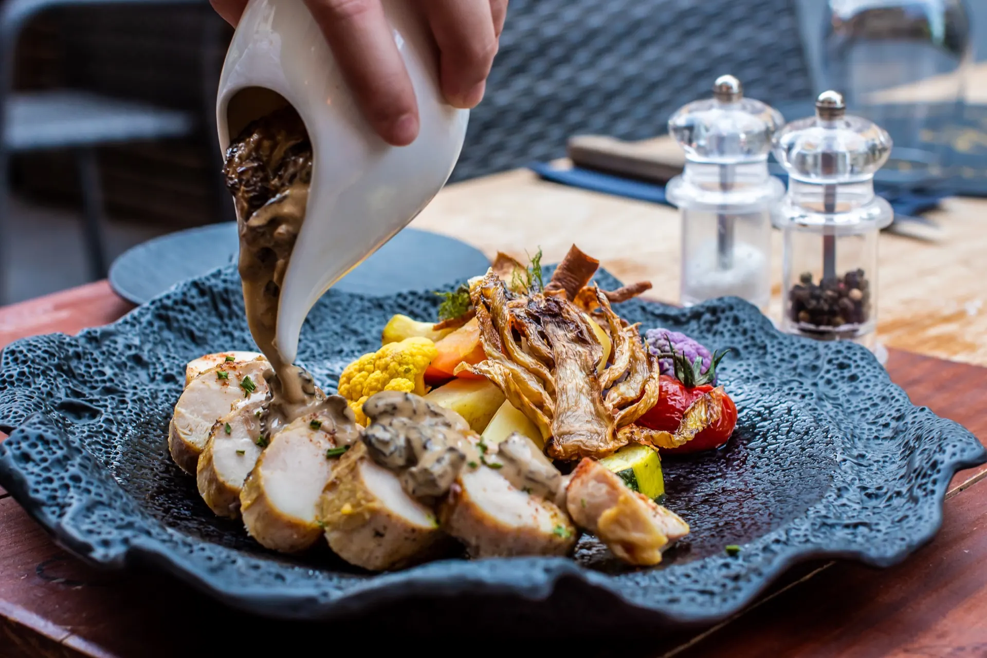 Sauce versée sur un suprême de volaille et ses légumes, dressé sur ardoise